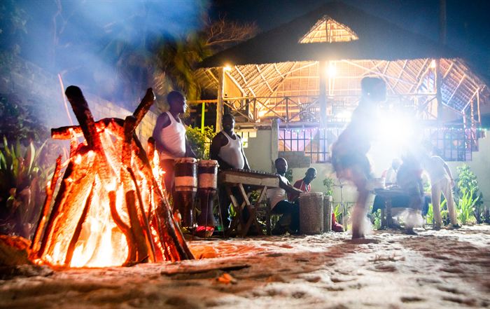 Drummers playing beside a bonfire at night under a thatched shelter, Tanzania