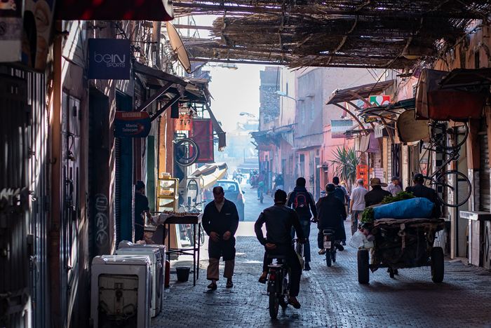 Pedestrians, a cyclist and a loaded handcart in a narrow covered street in the medina of Marrakech, Morocco