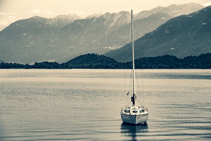 A single moored sailboat on a still lake below layered mountains, toned blue