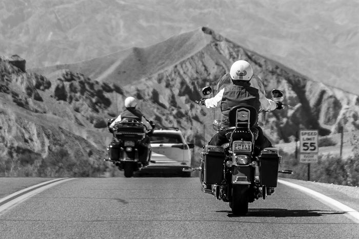 Two motorcyclists riding a desert highway seen from behind, mountains ahead, black and white